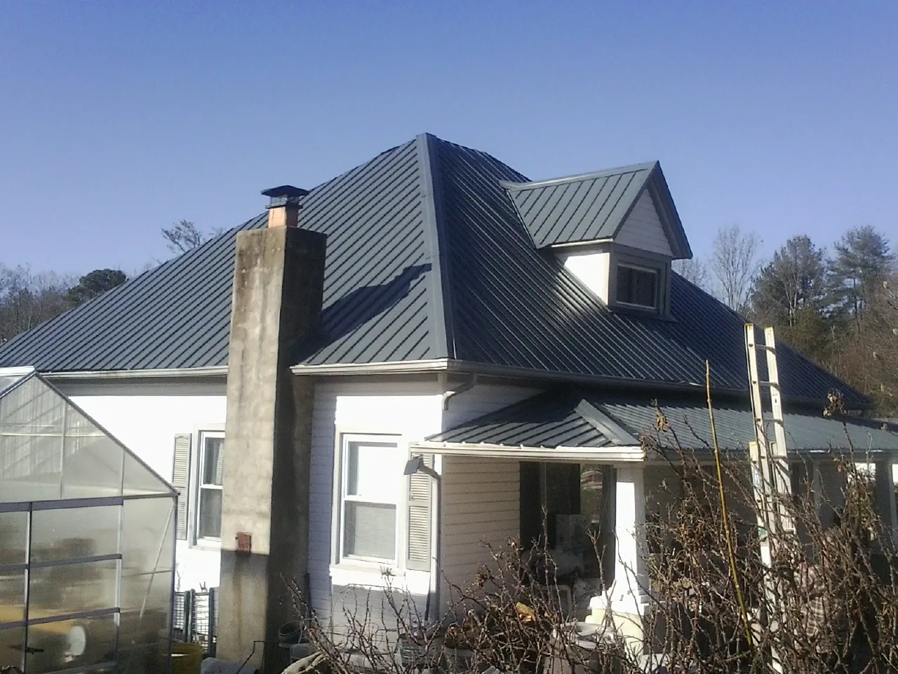 Dark blue standing seam metal roof on a white farmhouse with dormer — Slate & Tile Roof Repair by Roofing Brothers in Conesville