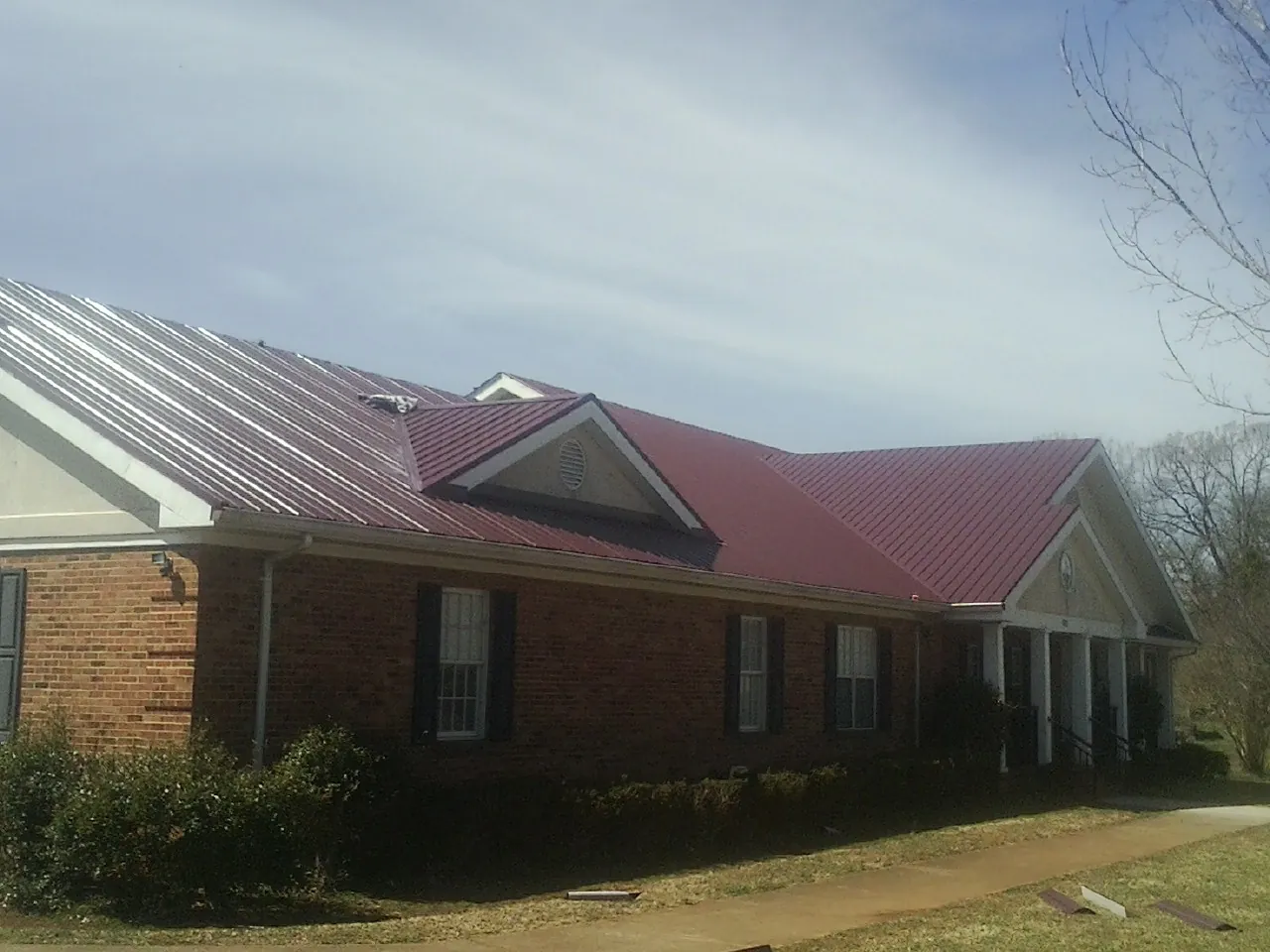 Red metal roof with gabled entries on a long brick building, from a Hail Damage Roof Repair job in Conesville