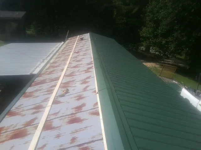 Old rusted panels beside newly installed green metal roofing — Wind Damage Roof Repair by Roofing Brothers in Conesville
