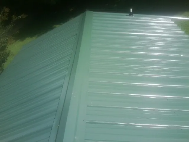 New green metal panels meeting at the ridge of a roof — Flat Roof Repair work by our crew in Conesville