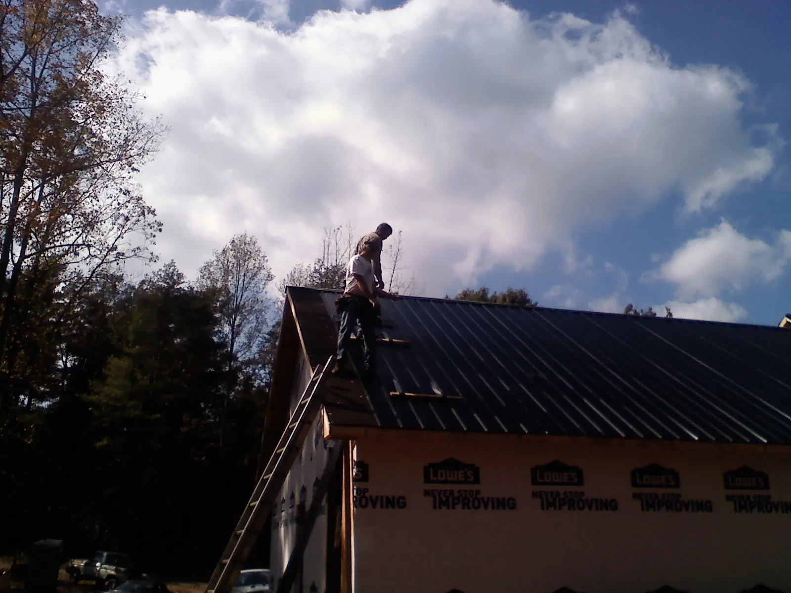 Roofer fastening dark metal panels high against a cloudy sky, from a Roof Inspection job in Conesville